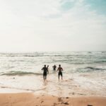 Three friends run into the ocean on a sunny day at a scenic beach in Bali.